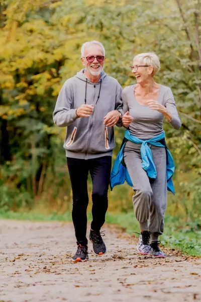 Starší pár běhá po lesní cestě a vyzařuje z něj vitalita, protože jejich praktické oblečení doplňuje svěží zelené stromy. Usmívající se pod jasným sluncem zanechávají za sebou všechny myšlenky na lékařskou ordinaci a zároveň si osvojují svůj aktivní životní styl.